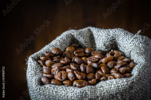 Сlose-up of bag of coarse canvas of coffee beans. Background with dark wood texture.