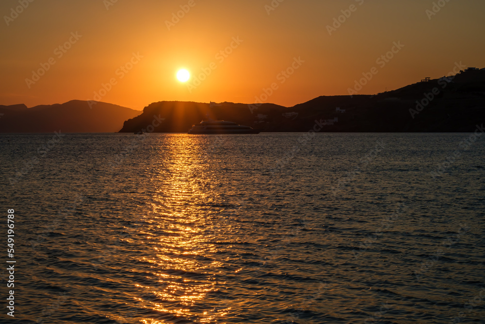 View of a sun bed, a sun umbrella and a stunning orange sunset at the beach of Mylopotas in Ios Greece