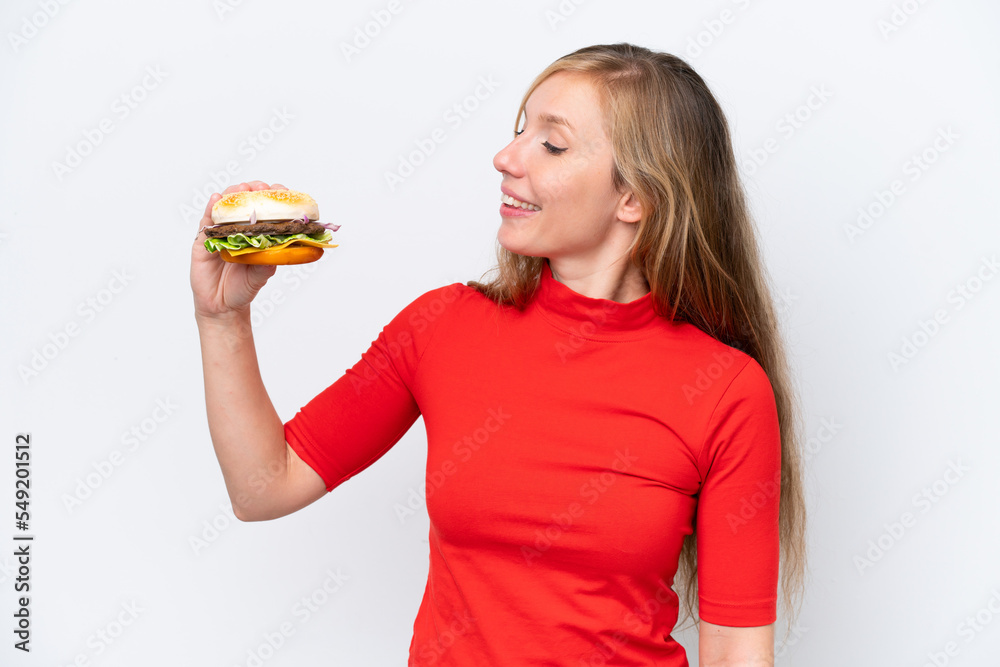 Young blonde woman holding a burger isolated on white background with happy expression Young blonde woman holding a burger isolated on white background with happy expression