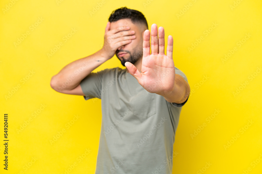 Young Arab handsome man isolated on yellow background making stop gesture and covering face Young Arab handsome man isolated on yellow background making stop gesture and covering face