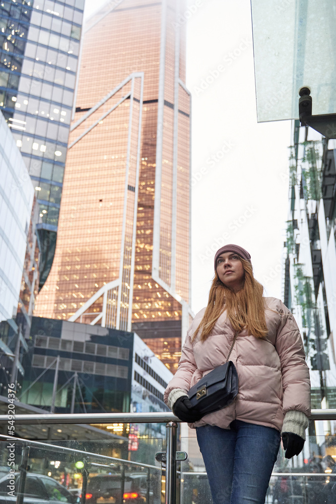 young woman next to skyscrapers and skyscrapers of a big city. tall business centers in the clouds in the background. bottom view