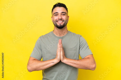 Young Arab handsome man isolated on yellow background keeps palm together. Person asks for something