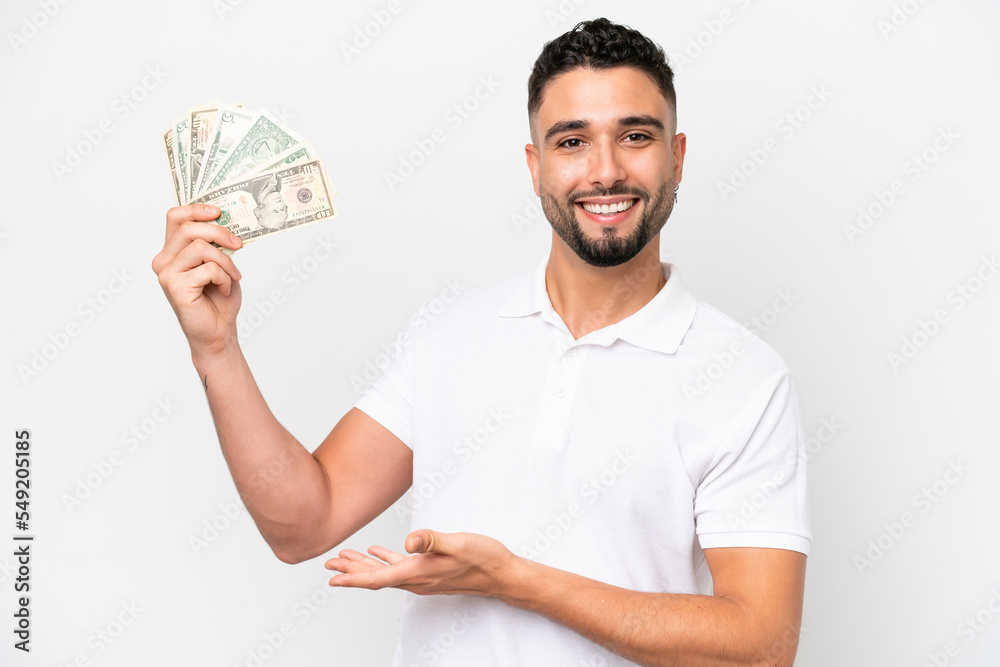 Young Arab man taking a lot of money isolated on white background extending hands to the side for inviting to come Young Arab man taking a lot of money isolated on white background extending hands to the side for inviting to come