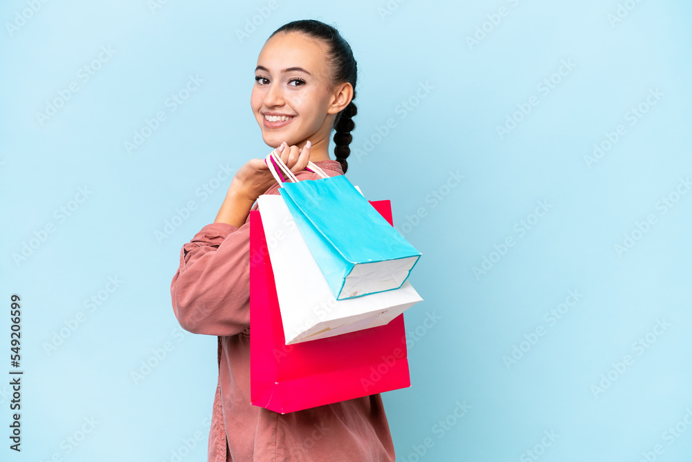 Young Arab woman isolated on blue background holding shopping bags and smiling Young Arab woman isolated on blue background holding shopping bags and smiling