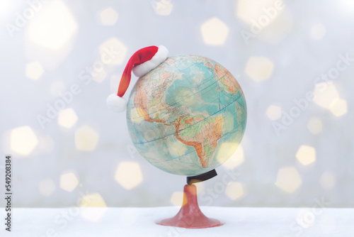 globe with christmas hat on snow. bokeh flare Santa Claus Hat as travel concept