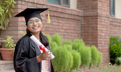 Happy young indian graduate girl student holding graduation degree on convocation ceremony. 