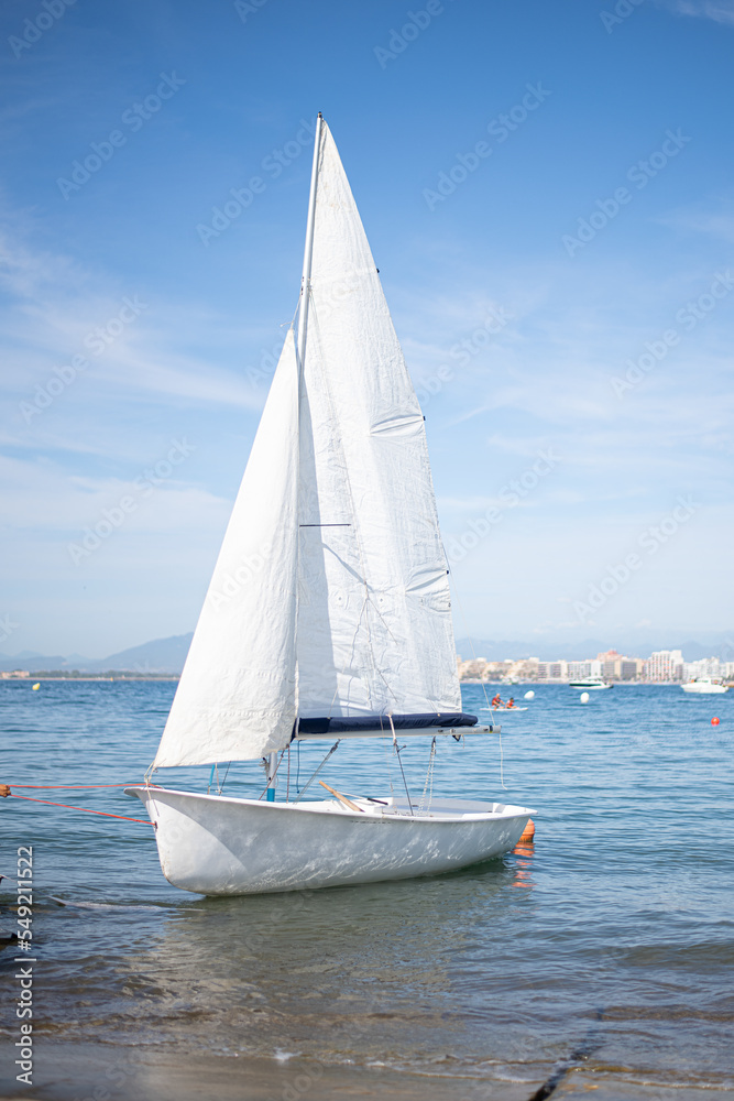 Obraz premium small white sailboat with white sails moored near the beach