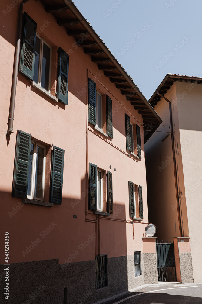 Old historic Italian architecture. Traditional European old town buildings. Wooden windows, shutters and pastel coral walls with sunlight shadows. Aesthetic summer vacation travel background