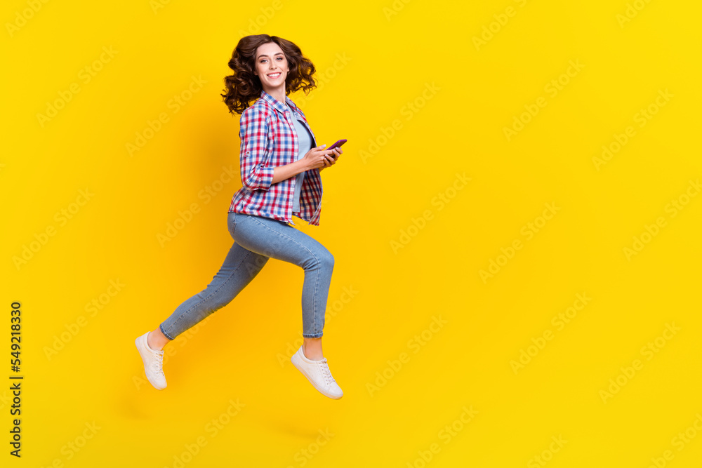 Full length photo of positive girl with wavy hairdo checkered shirt hold phone fast online delivery isolated on yellow color background