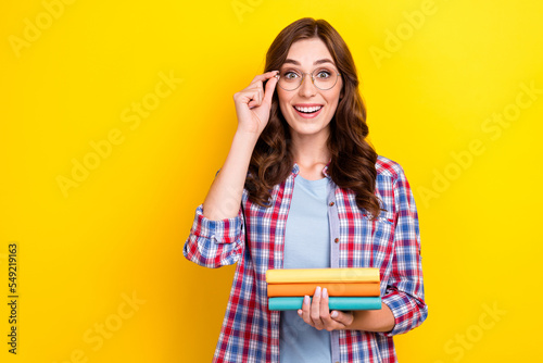Photo of impressed clever girl with wavy hairdo dressed checkered shirt hold book touch glasses isolated on yellow color background
