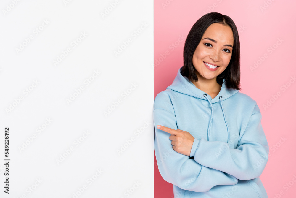 Photo of sweet adorable lady wear blue hoodie pointing finger blank billboard empty space isolated pink color background Photo of sweet adorable lady wear blue hoodie pointing finger blank billboard empty space isolated pink color background