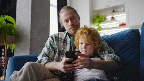 Young father and preschooler boy look at phone smiling photo