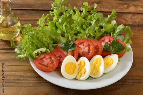 lettuce, tomato, egg and caper salad on a white plate on a wooden board