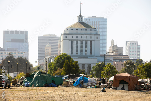A homeless encampment frames the skyline of downtown Oakland, California, USA.