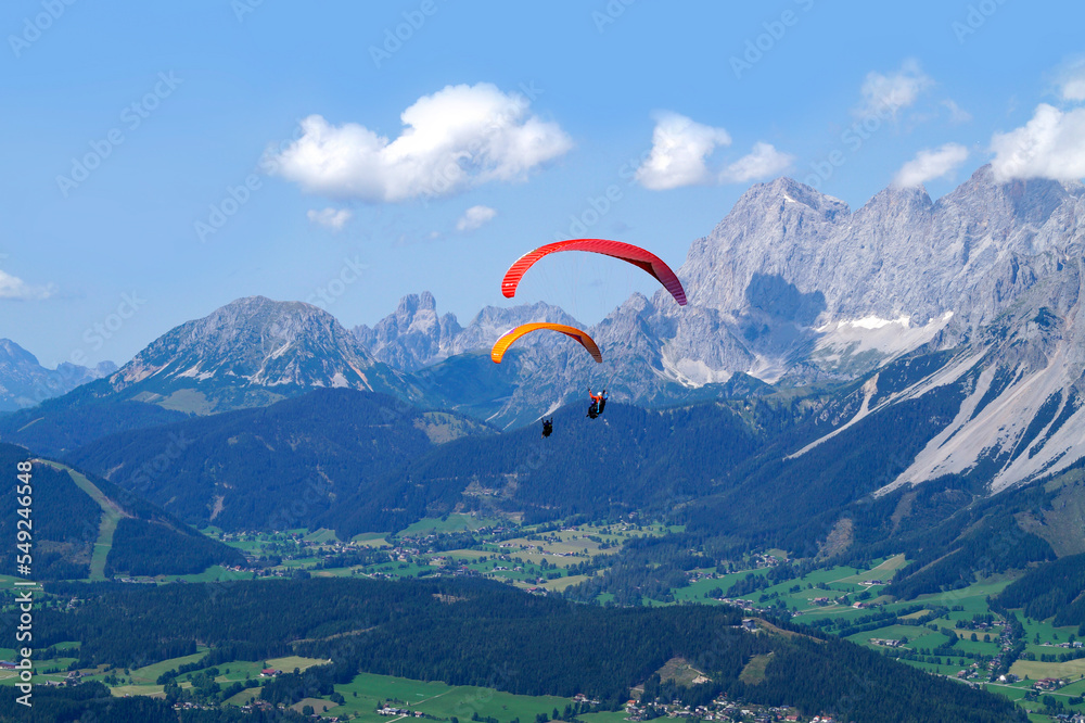 paragliders flying over the vast alpine valley surrounded by the Austrian Alps of the Schladming-Dachstein region on a sunny summer day (Schladming, Austria) paragliders flying over the vast alpine valley surrounded by the Austrian Alps of the Schladming-Dachstein region on a sunny summer day (Schladming, Austria)