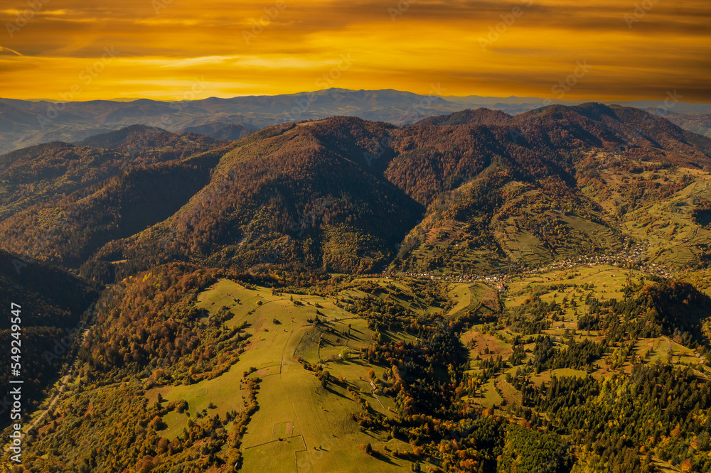 Beautiful autumn forest in the Carpathian mountains with orange sky on a autumn day on the Synevyr Pass ridge and blue sky background. Ukraine, drone view