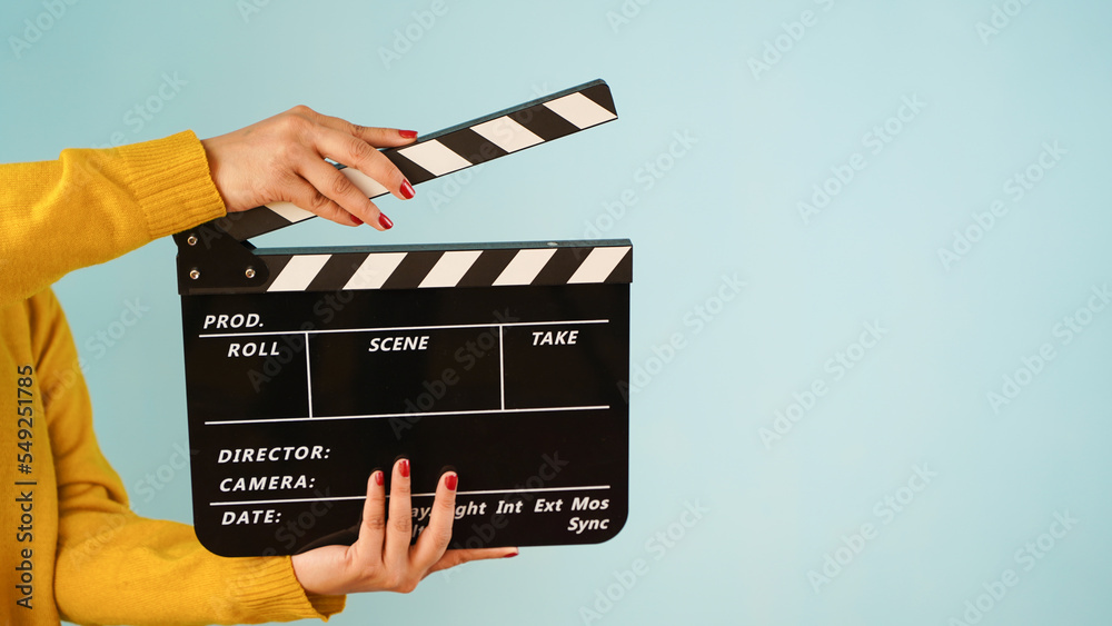 Hand is holding clapper board or clapperboard or movie slate, used in film production and cinema ,movies industry isolated over blue background.