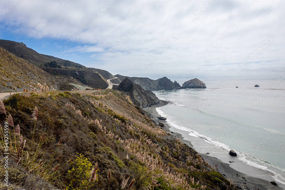 The beautiful west coast of California along Highway 1, with meadows and rocks, a blue sky and sea, with the remnants of fog in the distance
