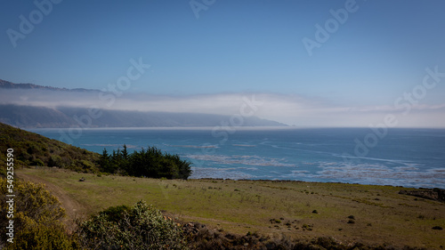 The beautiful west coast of California along Highway 1, with meadows and rocks, a blue sky and sea, with the remnants of fog in the distance