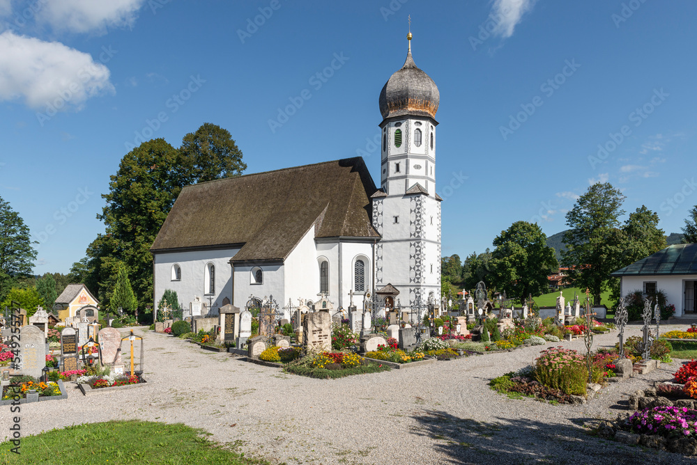 Die barocke katholische Kirche Mariä Schutz umgeben von Gräbern des Friedhofs von Fischbachau, Bayern, Deutschland