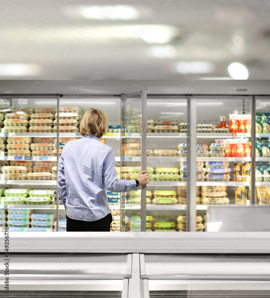  Man choosing frozen food from a supermarket freezer., reading product information