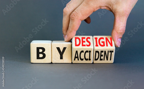 By accident and design symbol. Concept word By accident By design on wooden cubes. Beautiful grey table grey background. Businessman hand. Business by accident and design concept. Copy space.