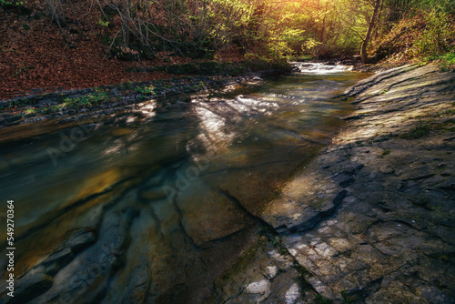 Amazing landscape mountain river in autumn forest at sunlight. View of stone water rapids and small waterfall.