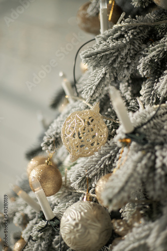 artificial lush cast snowy Christmas tree spruce decorated with white golden balls candles lights garland close up in white interior © MASTER111111
