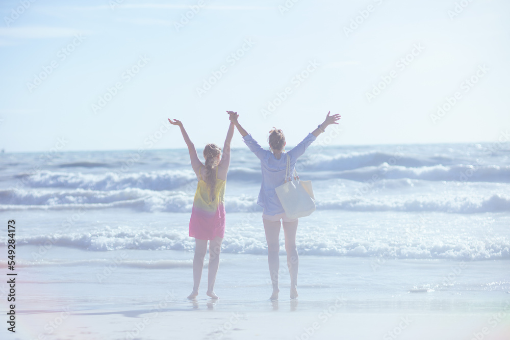 Seen from behind mother and teenage daughter at beach rejoicing Seen from behind mother and teenage daughter at beach rejoicing