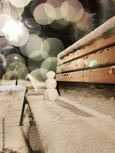 A small snowman on a bench covered with snow.