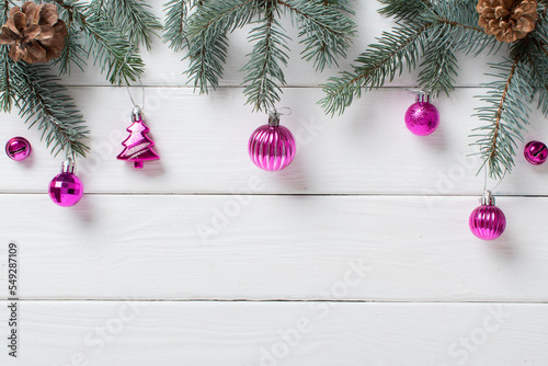Fir branches and pink Christmas decorations on a white wooden background.
