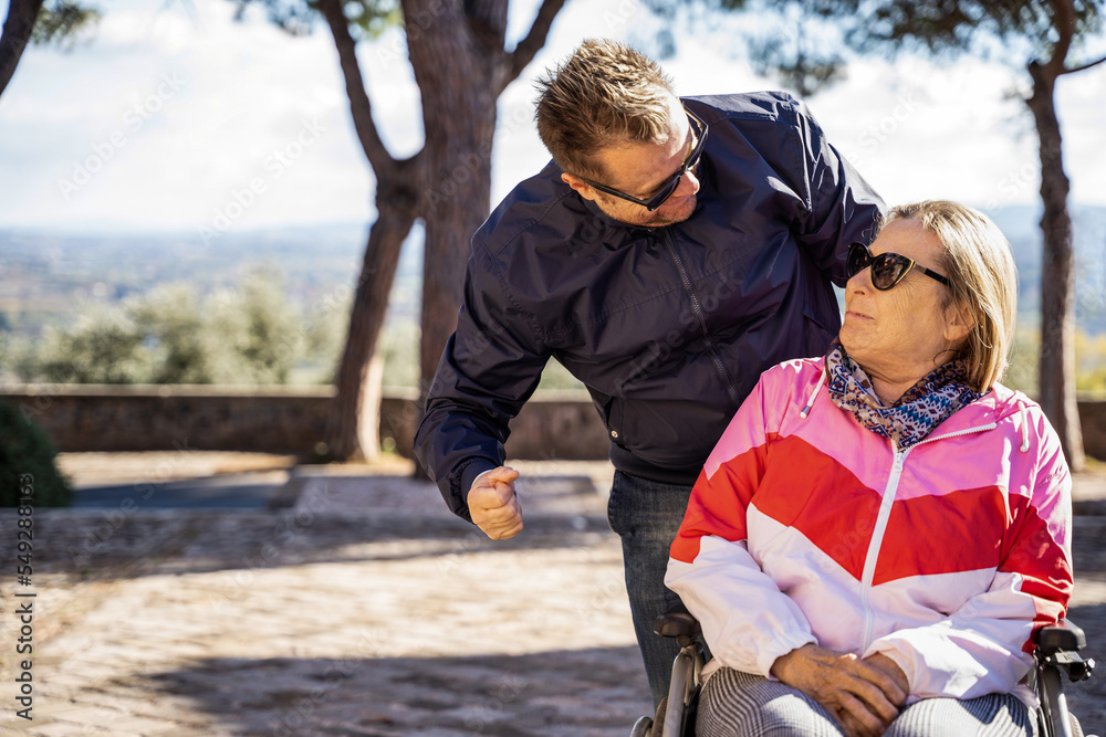 Disabled woman on wheelchair with man at park - Happy family having fun together outdoors - Son and Mother looking each other - Warm filter Disabled woman on wheelchair with man at park - Happy family having fun together outdoors - Son and Mother looking each other - Warm filter