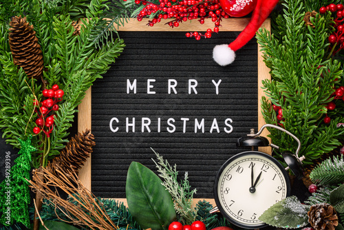 Letter board with words Merry Christmas, vintage clock, fir tree branches, red berries and decorations. Winter Christmas celebration concept. photo