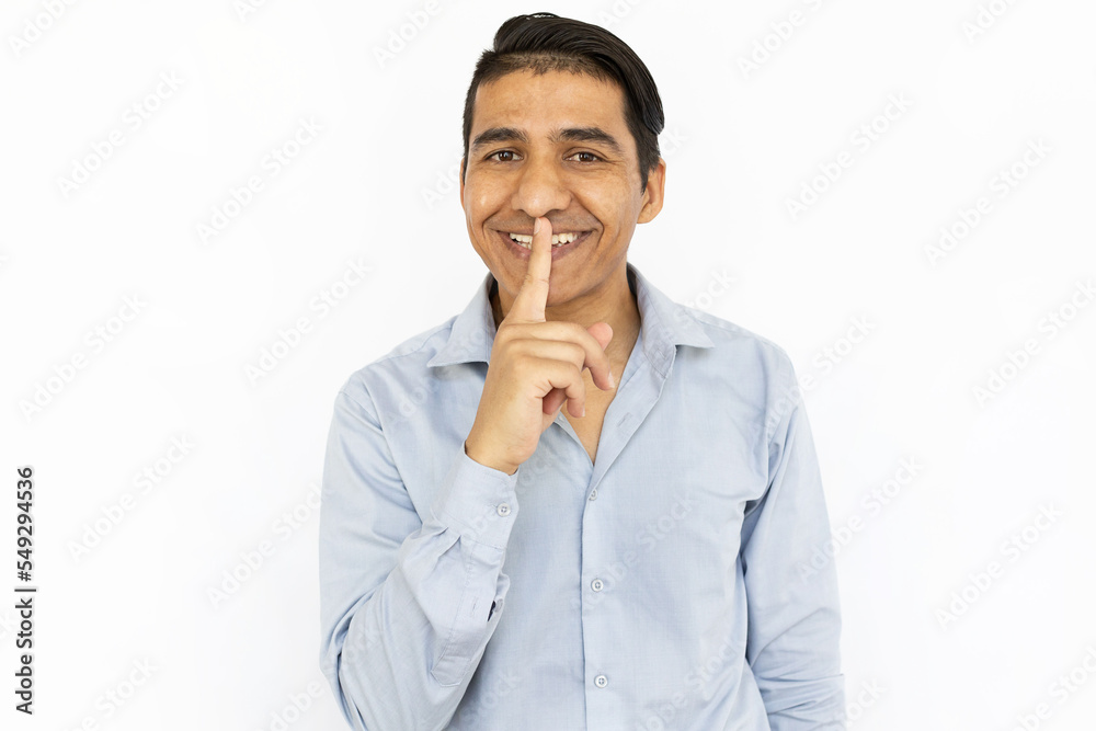 Happy Asian man making silence gesture. Man standing against white background, asking to be quiet, smiling and looking at camera. Silence, tranquility, secrecy concept