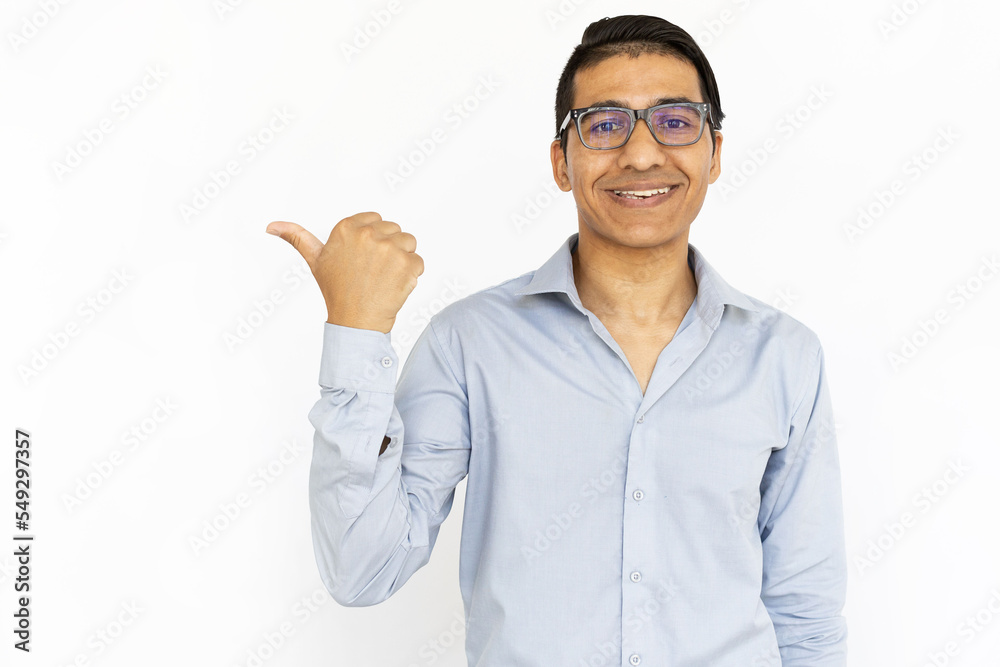 Satisfied man pointing with thumb. Indian man in blue shirt presenting product or app. Portrait, studio shot, advertising concept Satisfied man pointing with thumb. Indian man in blue shirt presenting product or app. Portrait, studio shot, advertising concept