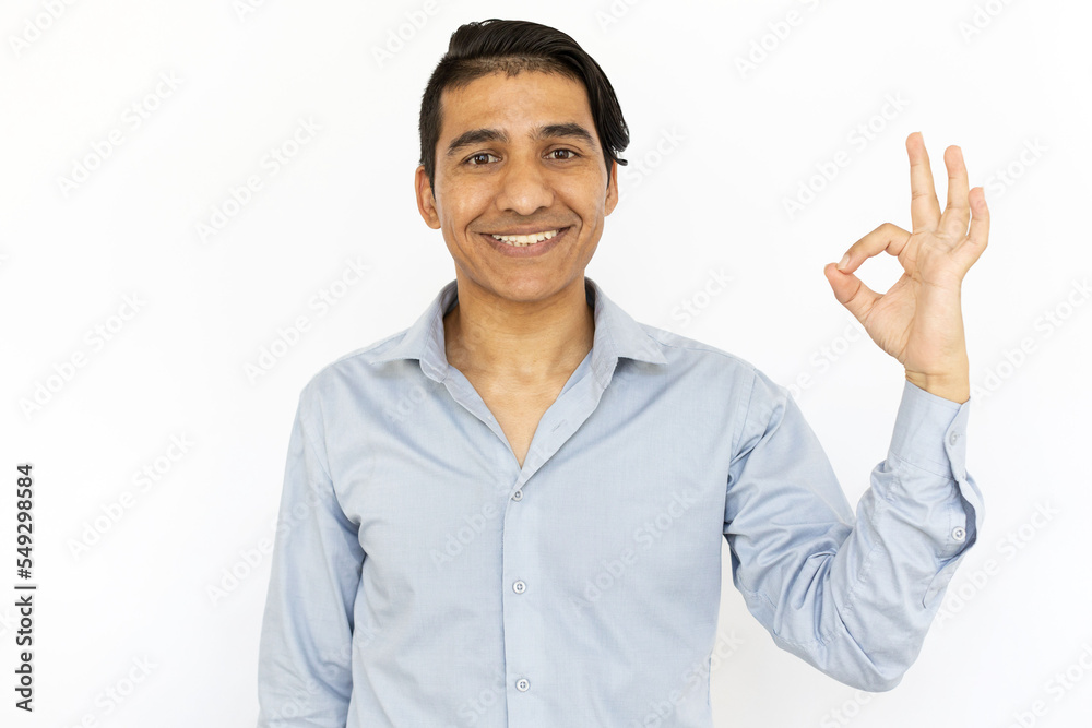 Smiling man showing OK sign at camera. Caucasian man standing against white background, looking at camera, making approving gesture. Satisfaction, happiness, concept Smiling man showing OK sign at camera. Caucasian man standing against white background, looking at camera, making approving gesture. Satisfaction, happiness, concept