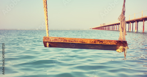Wooden swing above the water, selective focus, color toning applied.
