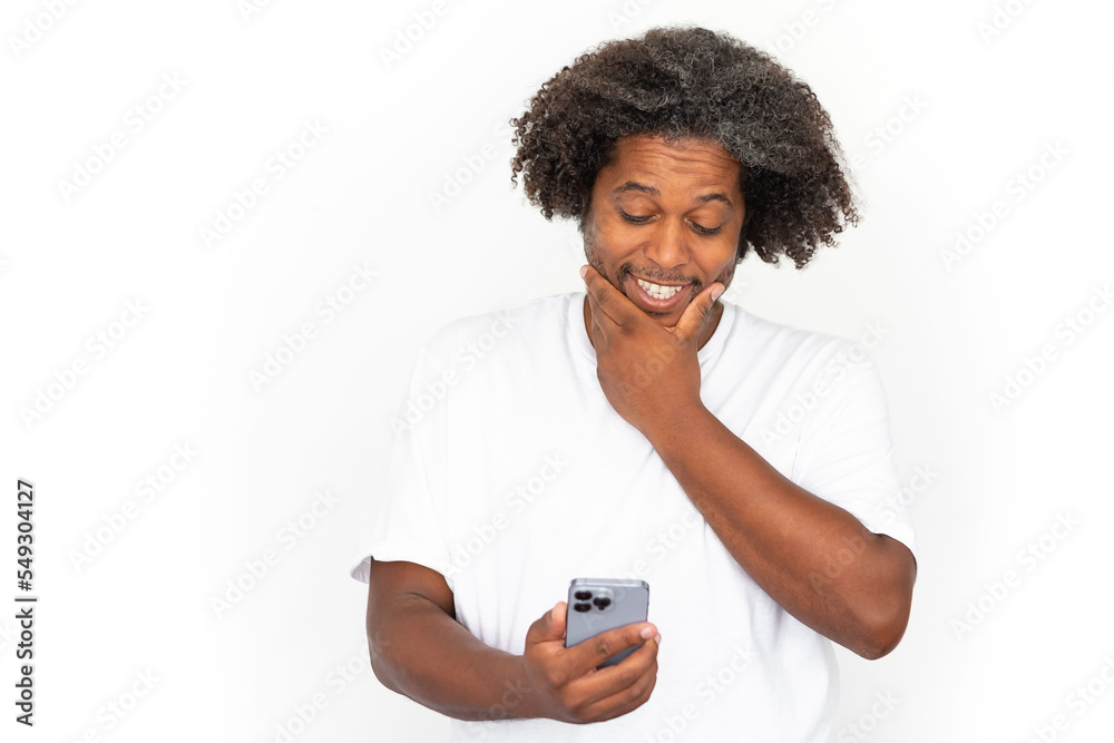 Thoughtful African American man using phone. Portrait of happy mature male model with dark curly hair in white T-shirt looking at screen, rubbing chin. Communication, modern technology concept Thoughtful African American man using phone. Portrait of happy mature male model with dark curly hair in white T-shirt looking at screen, rubbing chin. Communication, modern technology concept