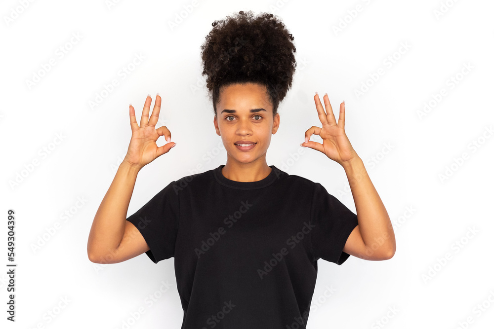Portrait of happy young woman making okay gesture. African American woman wearing black T-shirt looking at camera and smiling against white background. Success and satisfaction concept Portrait of happy young woman making okay gesture. African American woman wearing black T-shirt looking at camera and smiling against white background. Success and satisfaction concept