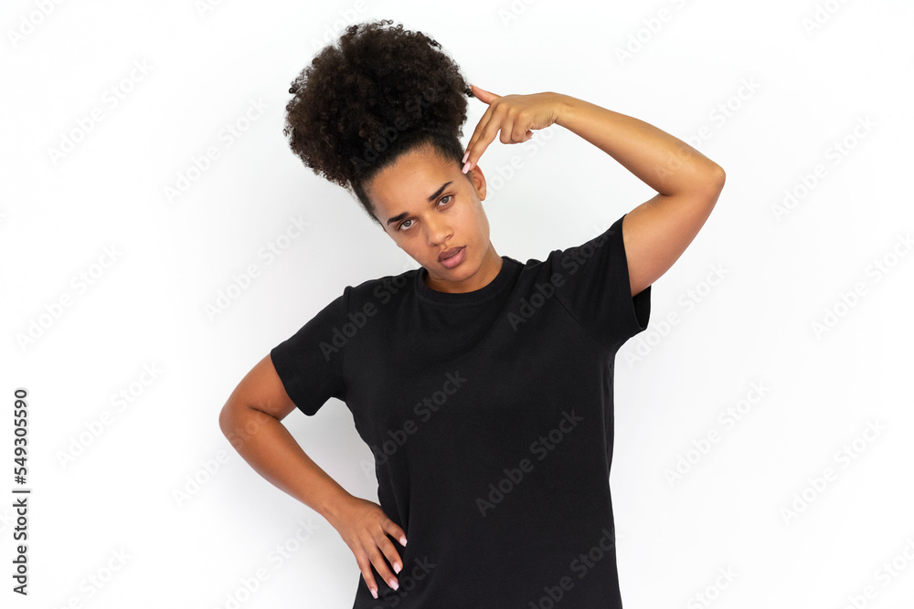 Portrait of tired young woman making suicide gesture against white background. African American woman wearing black T-shirt looking at camera in exhaustion. Stress concept Portrait of tired young woman making suicide gesture against white background. African American woman wearing black T-shirt looking at camera in exhaustion. Stress concept