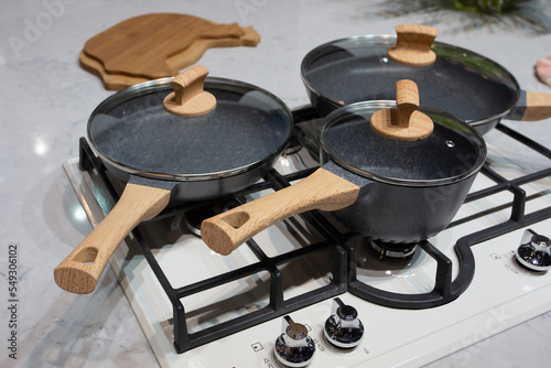 Classic set of kitchen utensil with black pan, saucepan and pot with glass lids, on the white traditional  gas stove. Photo with selective focus