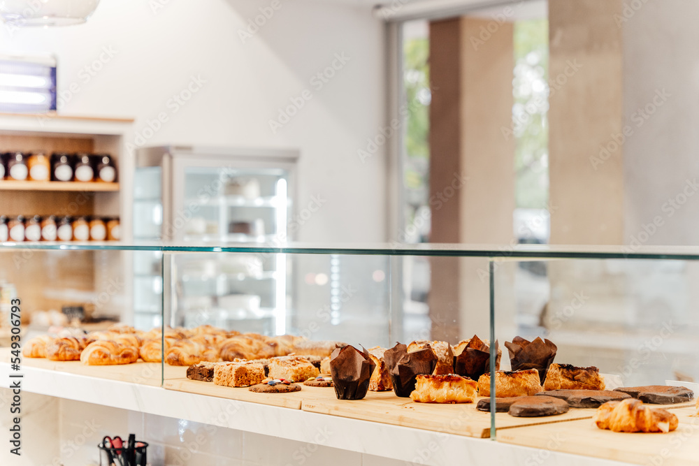 Homemade croissants, muffins, cupcakes and other pastry at a bakery on wooden tables and glass cover