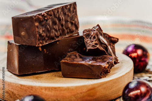 Chocolate, rice and nut Christmas nougat over a wooden plate on a white background with decorations