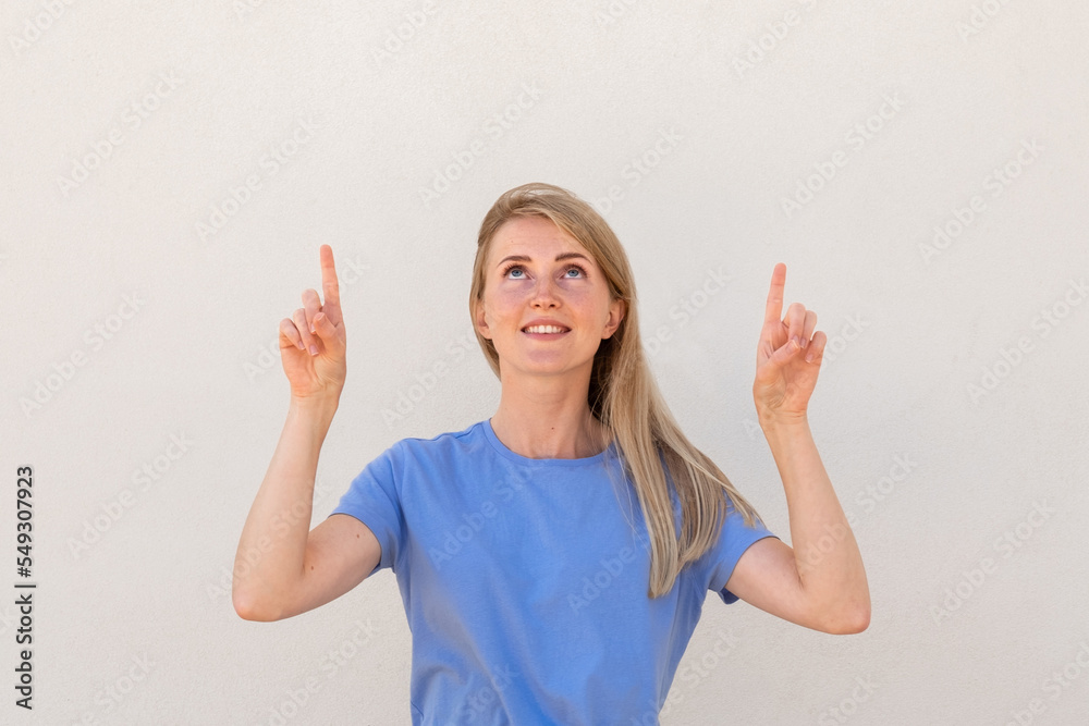 Cheerful young woman pointing with fingers above at copyspace. Caucasian female model with blonde hair and blue eyes in casual clothes presenting advertisement. Advertising, social media concept Cheerful young woman pointing with fingers above at copyspace. Caucasian female model with blonde hair and blue eyes in casual clothes presenting advertisement. Advertising, social media concept