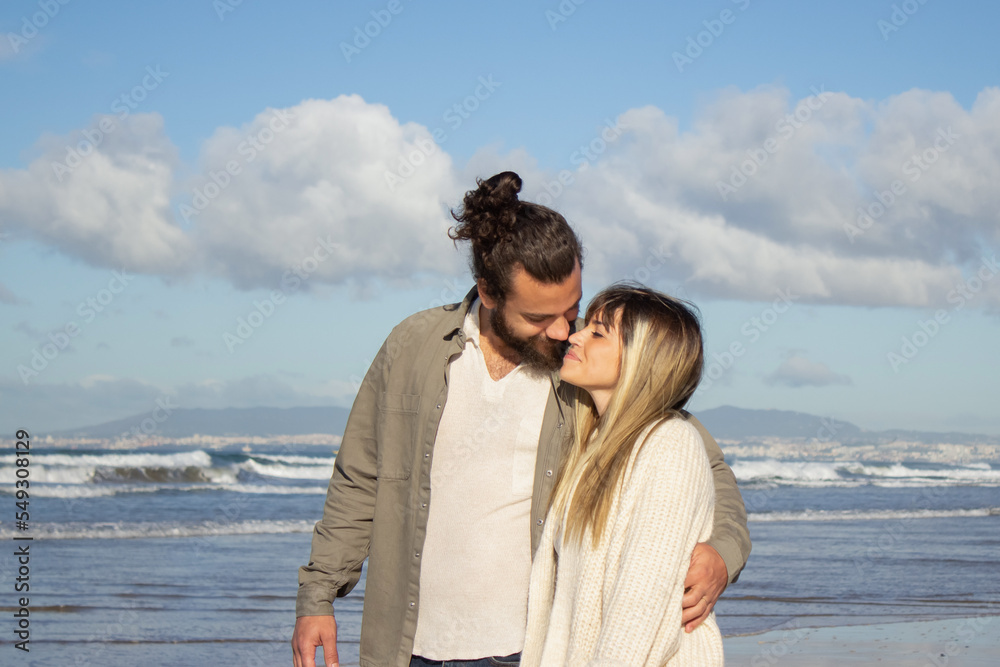 Loving couple walking near water on summer day. Bearded man and woman in casual clothes being tender, cuddling. Love, travelling, dating concept