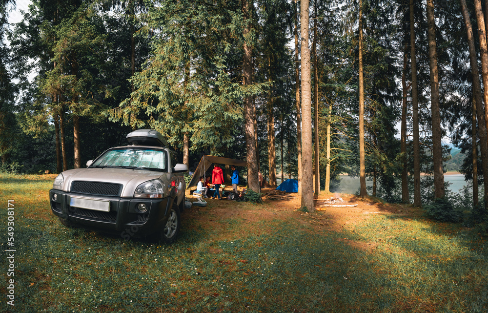 Camp, camping in wilderness. Travel and tourism by car. Vehicle near tall coniferous trees. Tents and active recreation in the Carpathian Mountains