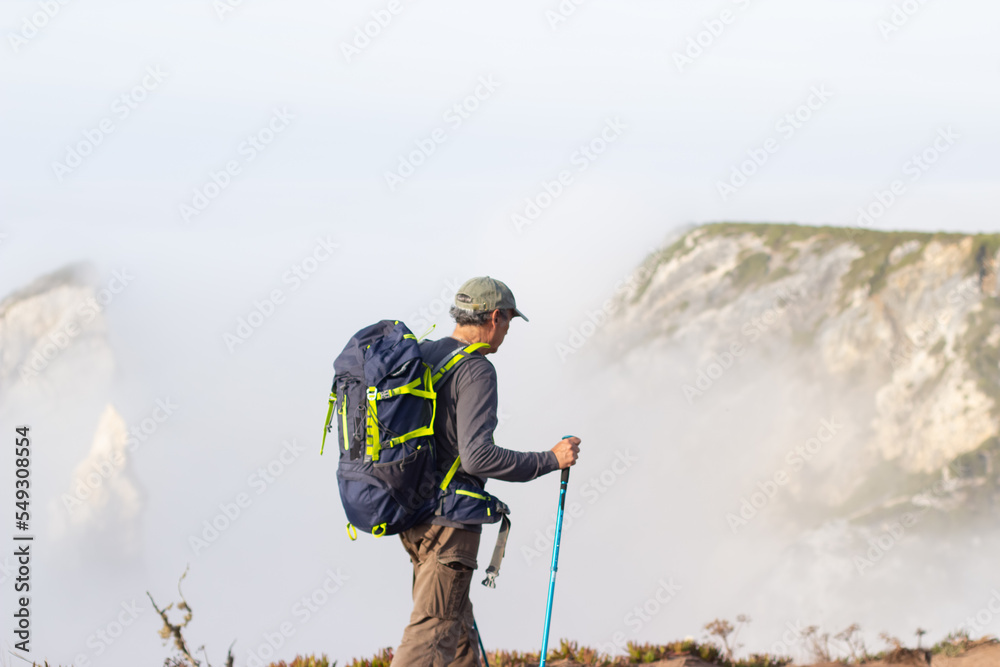 Obraz premium Side view of elderly man hiking on foggy day. Sportsman with backpack going uphill. Leisure, sport concept