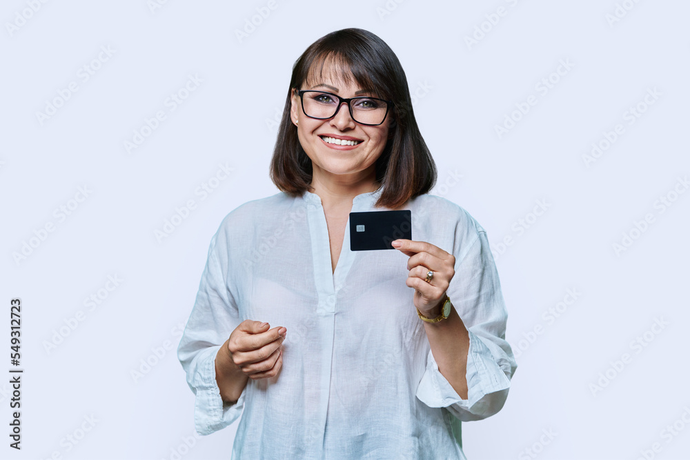 Attractive middle aged smiling woman holding plastic credit card, white background Attractive middle aged smiling woman holding plastic credit card, white background