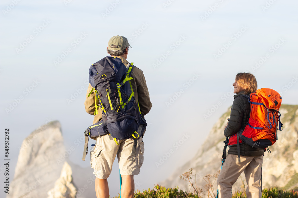 Back view of elderly family hiking on summer. Man and woman in casual clothes and with ammunition looking at each other. Hobby, active lifestyle concept