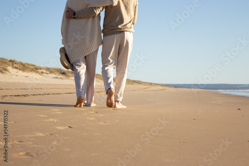 Romantic couple enjoying vacation at seaside while walking along beach and embracing. Back view of middle-aged man and woman spending holiday time together. Coastline background. Love, leisure concept